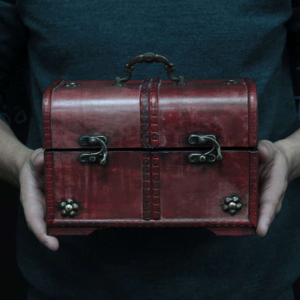 Red leather chest held by a person against a dark background