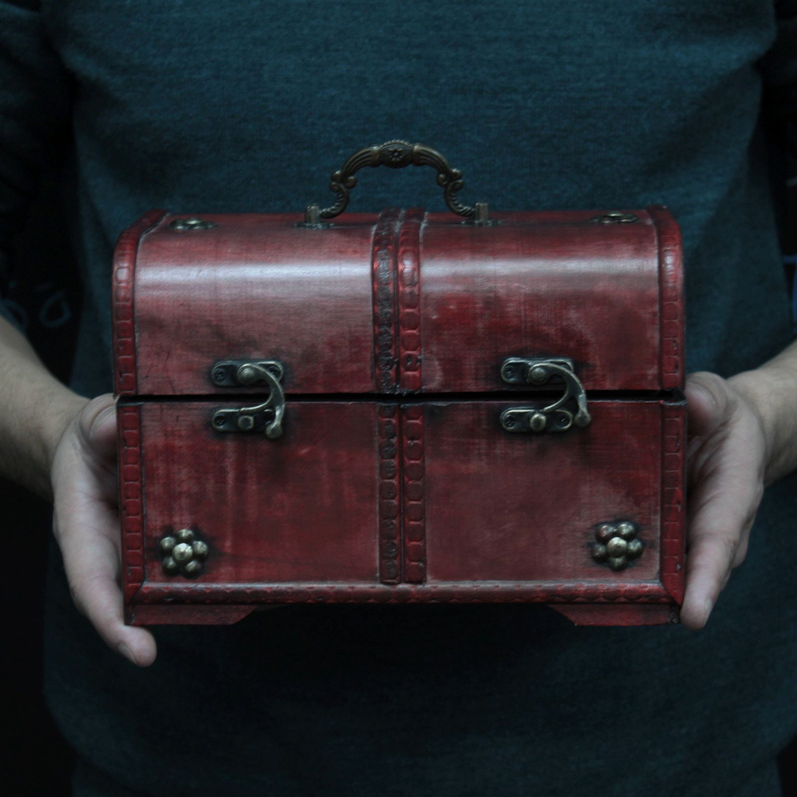 Red leather chest held by a person against a dark background